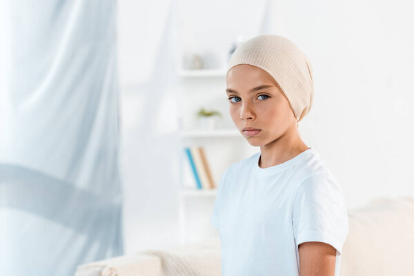 sick kid in head scarf looking at camera at home 