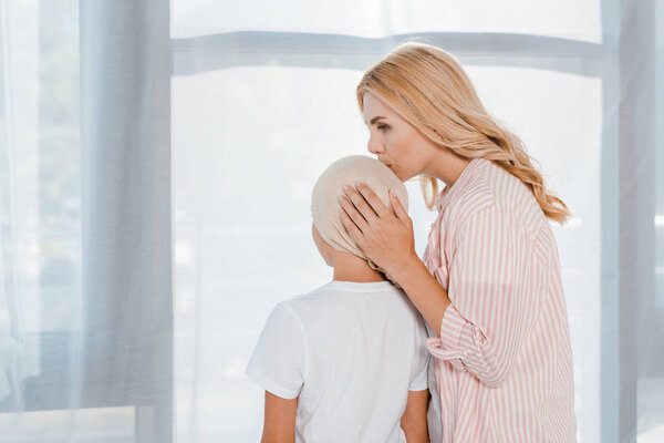 mother kissing sick child in head scarf at home 