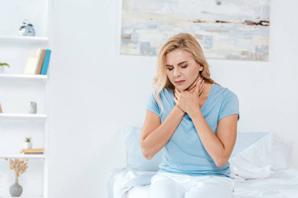 sick woman having sore throat while sitting on bed at home 