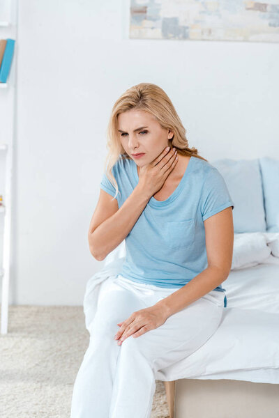 woman having sore throat while sitting on bed at home 