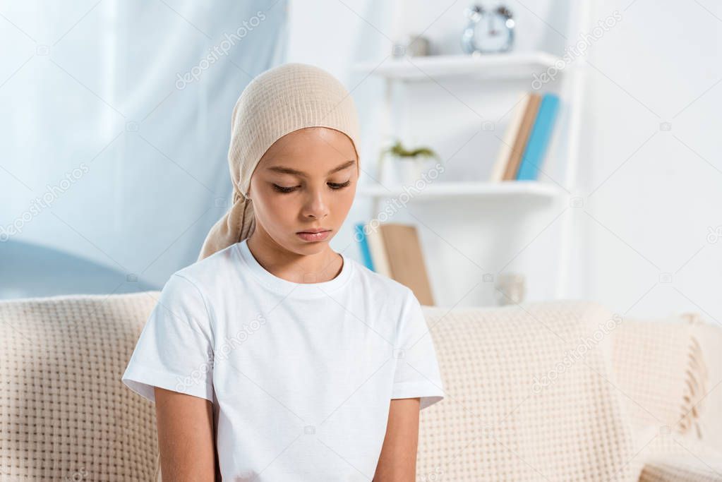 frustrated kid in head scarf sitting on sofa in living room 