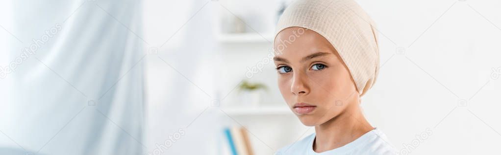 panoramic shot of sick kid in head scarf looking at camera