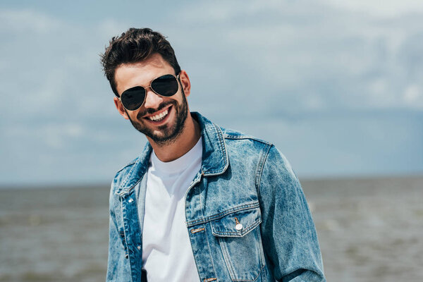 handsome man in denim jacket and sunglasses looking at camera 