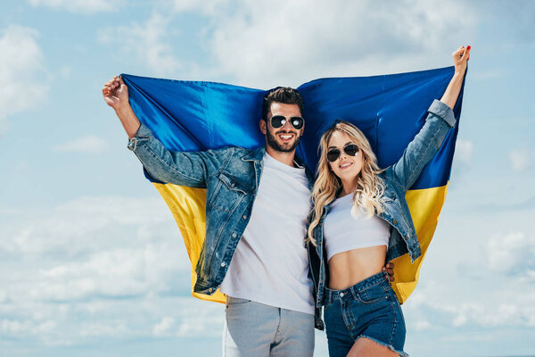привлекательная женщина и красивый мужчина улыбается и держит украинский флаг
 