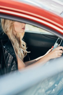 arabada oturan siyah ceketli sarışın kadın kırpılmış görünümü 