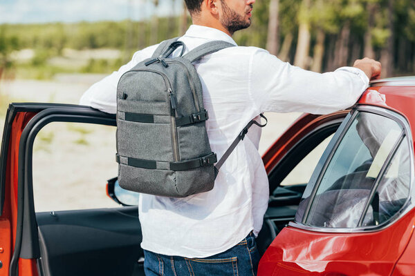 back view of man in shirt with backpack standing near car 