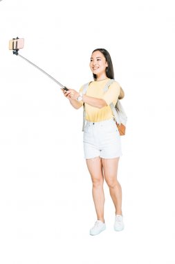 beyaz arka planda selfie çubuğu ile akıllı telefonda selfie çeken çekici asyalı kadın