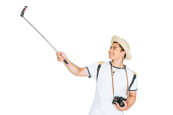 cheerful asian man taking selfie on smartphone with selfie stick isolated on white