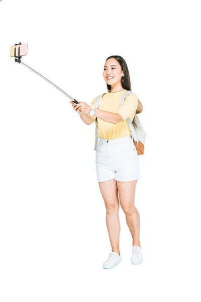 attractive asian woman taking selfie on smartphone with selfie stick on white background