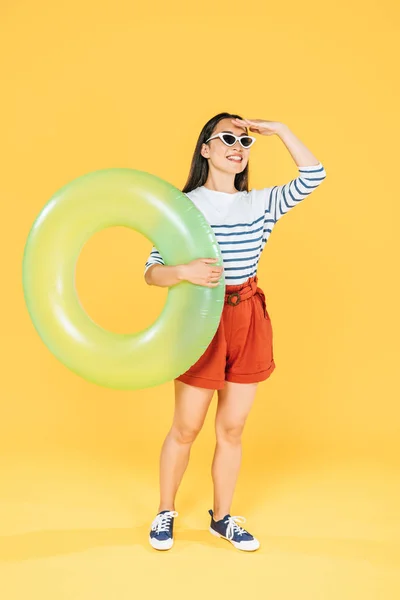 水泳の指輪を持ち 黄色の背景を見つめるサングラスをかけたかわいいアシンの女性 — ストック写真