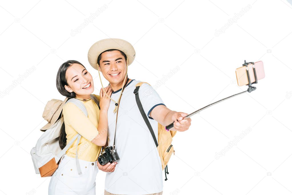 two happy asian tourists taking selfie on smartphone with selfie stick isolated on white