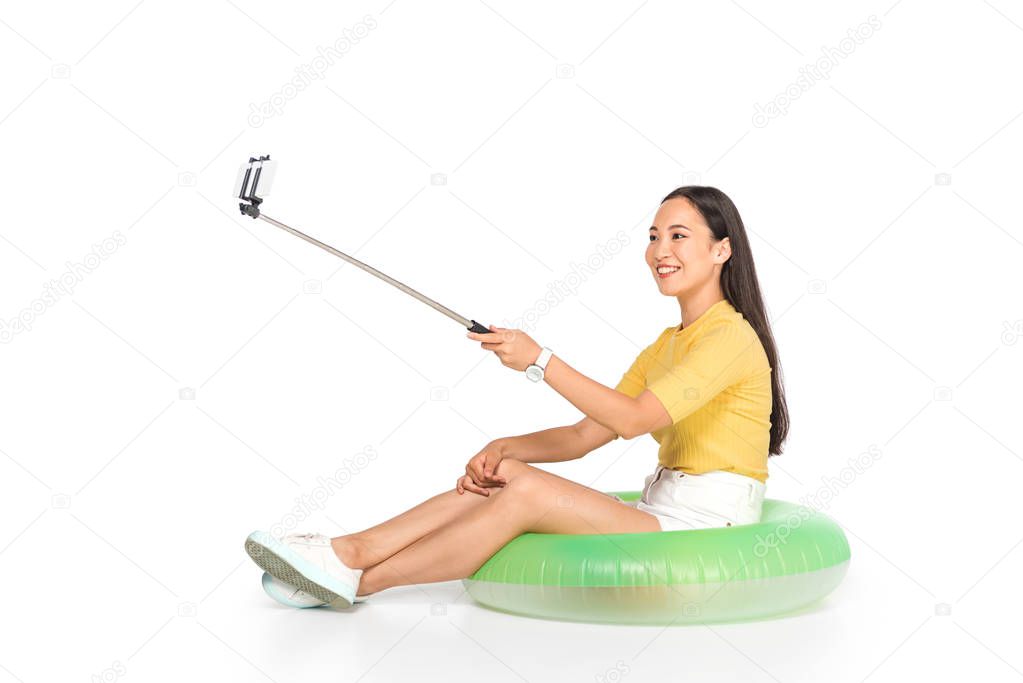 attractive asian woman taking selfie on smartphone with selfie stick on white background