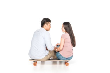 mutlu asyalı çift longboard üzerinde oturan ve beyaz arka plan üzerinde birbirlerine bakarak