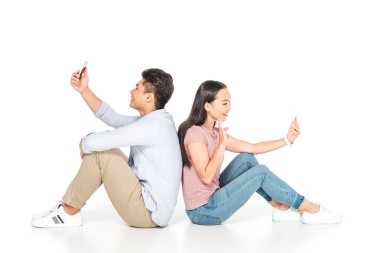 genç asyalı çift arka arkaya oturan ve beyaz arka plan üzerinde akıllı telefonlar kullanarak