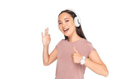 kulaklık müzik dinle güzel asyalı kadın, beyaz izole kamera gülümserken başparmak ve tamam jest gösteren