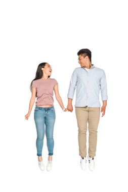 mutlu asyalı çift atlama ve beyaz arka plan üzerinde el ele tutuşurken birbirlerine bakıyor