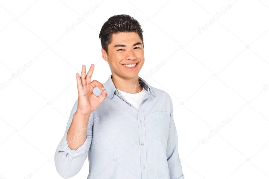 happy asian man showing okay sign while smiling at camera isolated on white