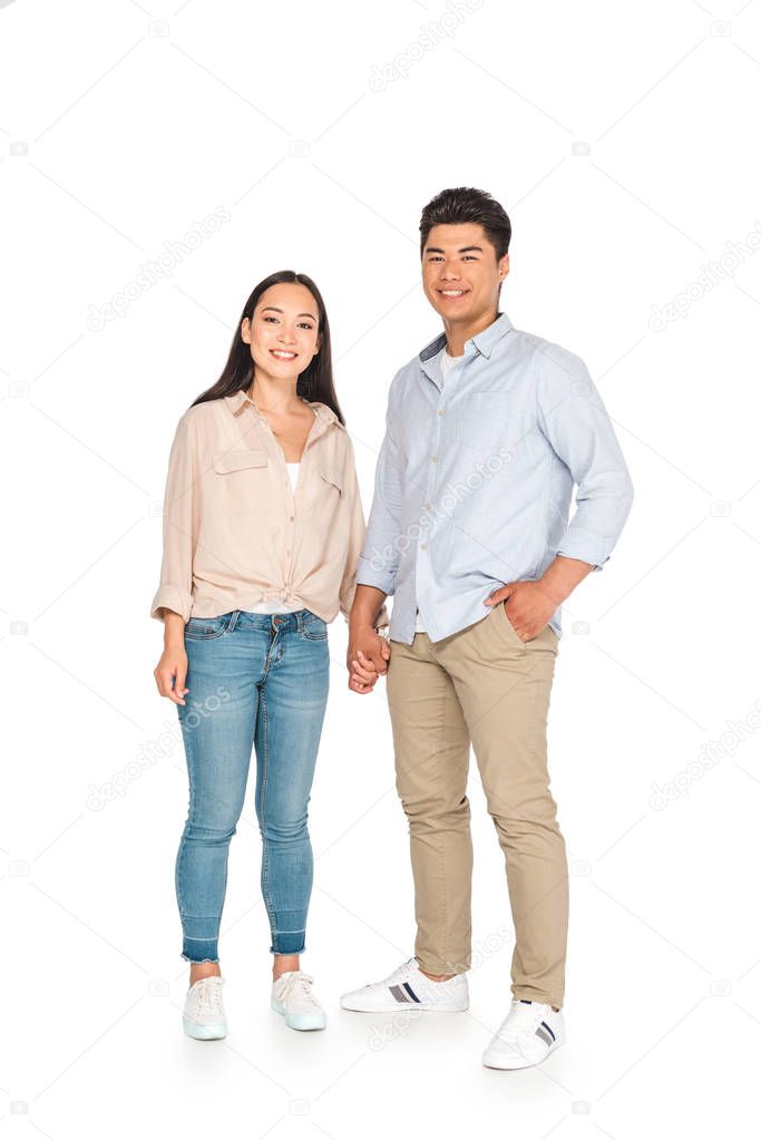 happy asian couple holding hands and smiling at camera on white background