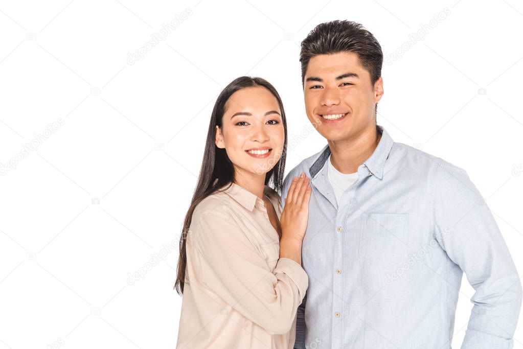 happy asian woman embracing handsome boyfriend while smiling at camera isolated on white