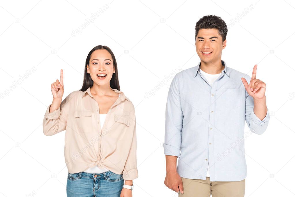 smiling asian man and woman showing idea signs while looking at camera isolated on white