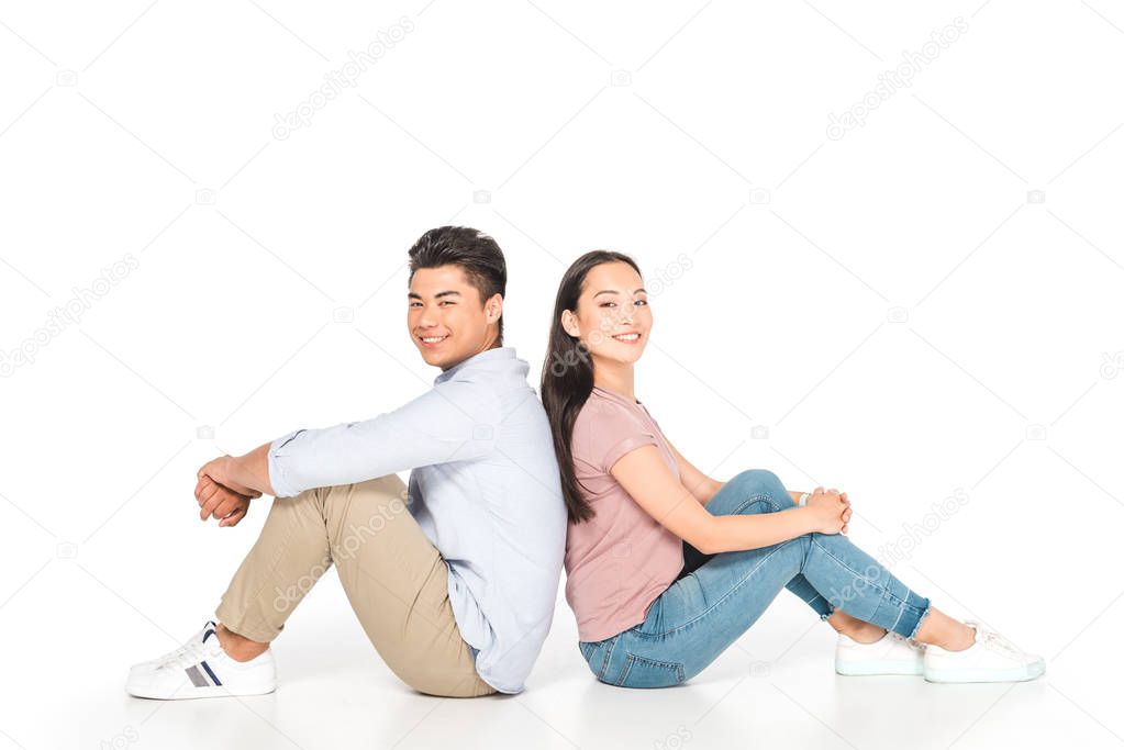 young asian couple sitting back to back and looking at camera on white background