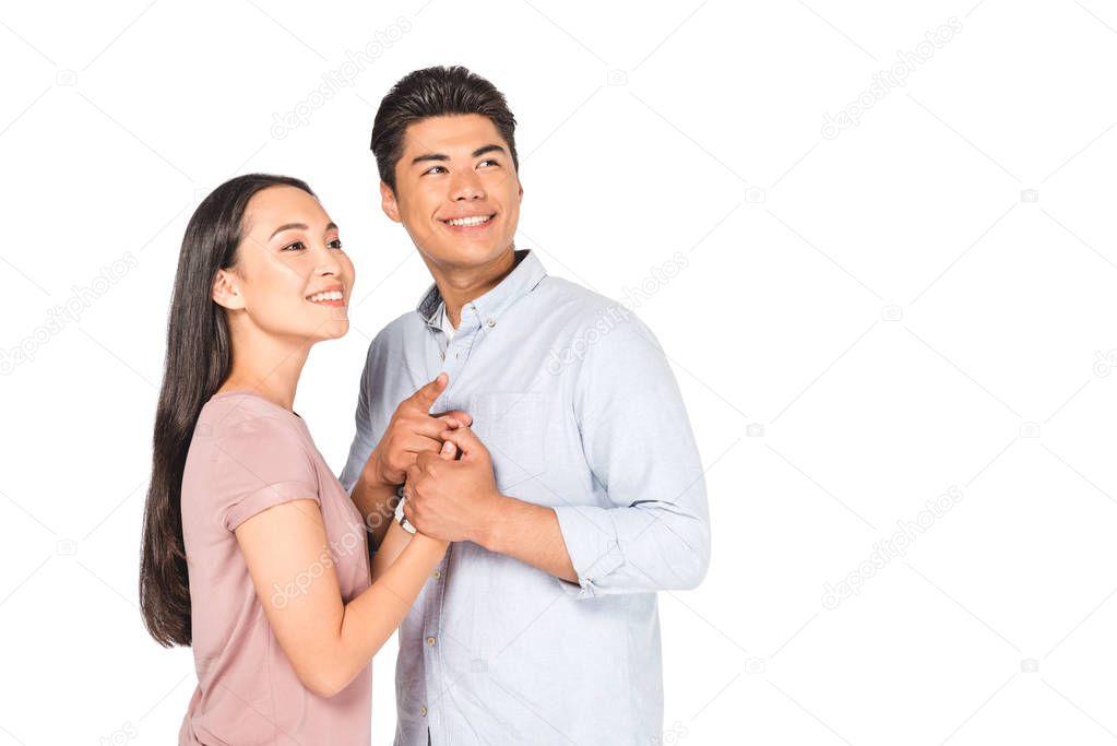 happy asian couple holding hands while smiling and looking away isolated on white