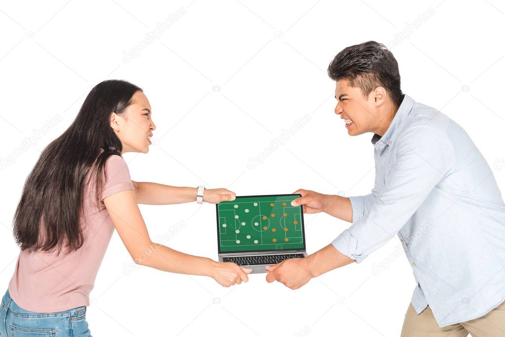 irritated asian man and woman holding laptop with football video game on screen isolated on white