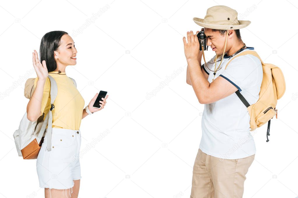 young asian tourists taking photo of girlfriend waving hand isolated on white