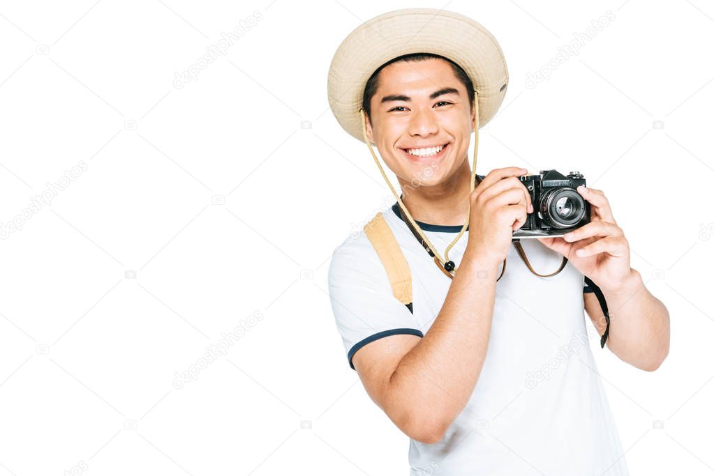 happy asian tourist in hat holding digital camera and smiling at camera isolated on white