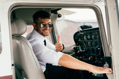 güneş gözlüğü gülümseyen yakışıklı pilot kameraya bakarak ve uçakta başparmak gösteren