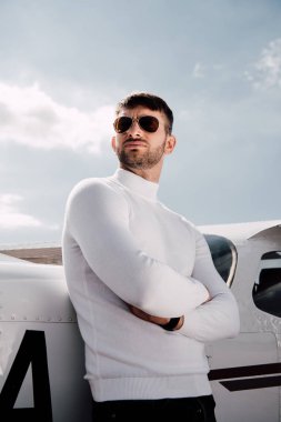 uçağın yanında çapraz kolları ile duran güneş gözlüğü ciddi adam düşük açı görünümü