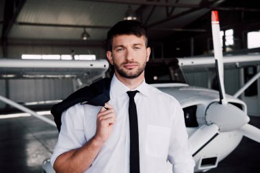 front view of serious pilot holding jacket and looking at camera clipart