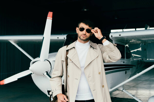 pensive stylish businessman in coat standing near plane