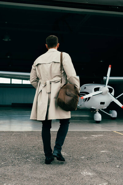 back view of stylish businessman in coat standing near plane