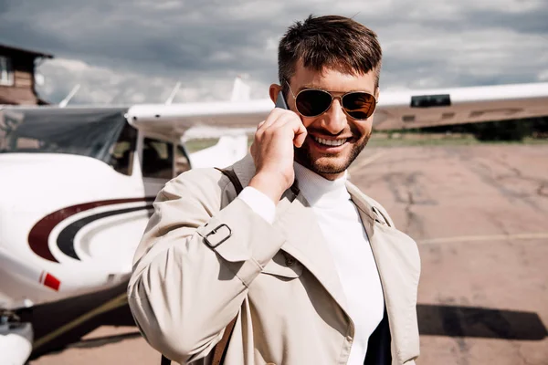 Hombre Sonriente Abrigo Con Bolsa Hablando Teléfono Inteligente Cerca Avión —  Fotos de Stock