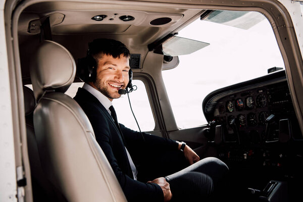 smiling bearded pilot in formal wear sitting in plane