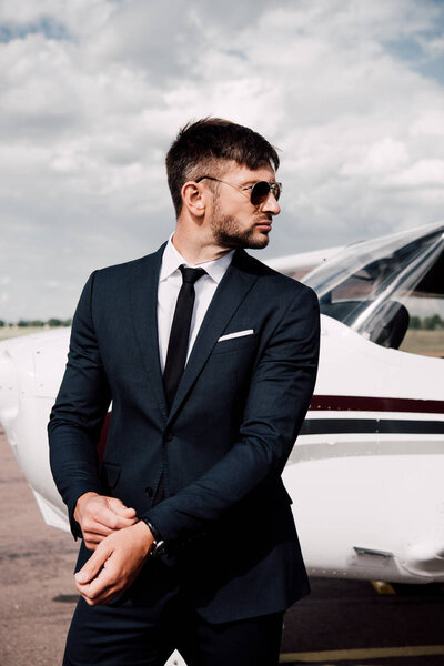 pensive businessman in formal wear standing near plane in sunny day