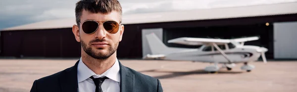 飛行機の近くに立っているフォーマルな服とサングラスで深刻なビジネスマンのパノラマショット — ストック写真