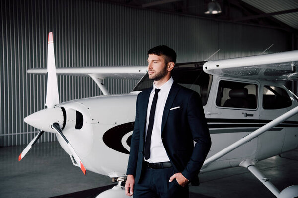 confident businessman in formal wear standing with hand in pocket near plane