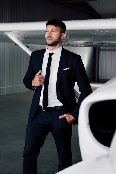 飛行機の近くにポケットに手で立ってフォーマルな服を着て自信のあるビジネスマン — ストック写真