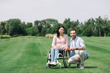 parkta genç engelli kız arkadaşı yakınında uçan disk tutan gülümseyen adam