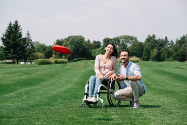 parkta genç engelli kız arkadaşı yakın uçan disk atma gülümseyen adam