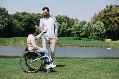 parkta gölet yakınında dinlenirken engelli kız arkadaşı ile el ele neşeli genç adam