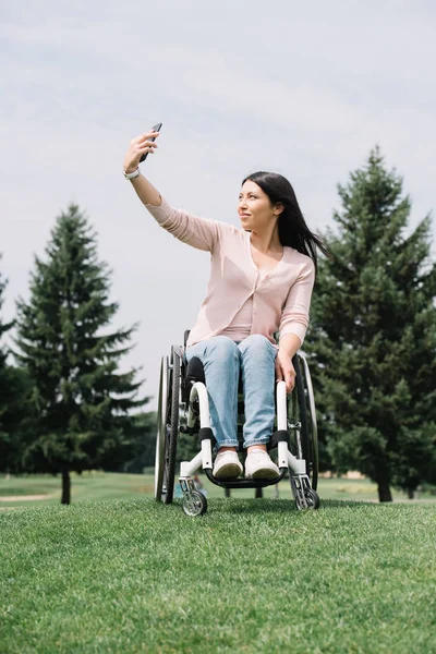 公園を歩きながらスマートフォンで自分撮りをする魅力的な障害のある女性 — ストック写真