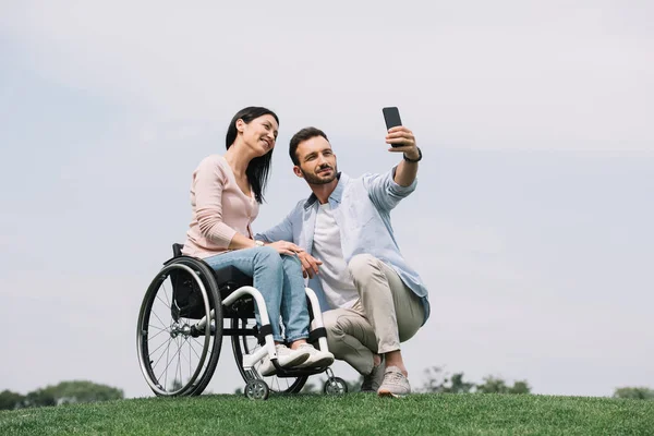 Szczęśliwy Młody Człowiek Biorąc Selfie Smartfonie Uśmiechniętą Dziewczyną Niepełnosprawnych Parku — Zdjęcie stockowe