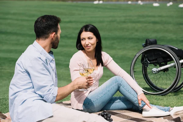 公園で毛布の上に座っている間 陽気な障害のある女性がボーイフレンドとワイングラスをクリンキング — ストック写真