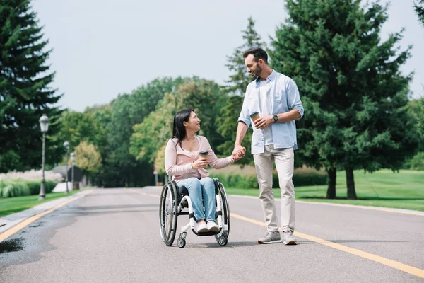 happy disabled woman holding hands with handsome boyfriend while walking in park together