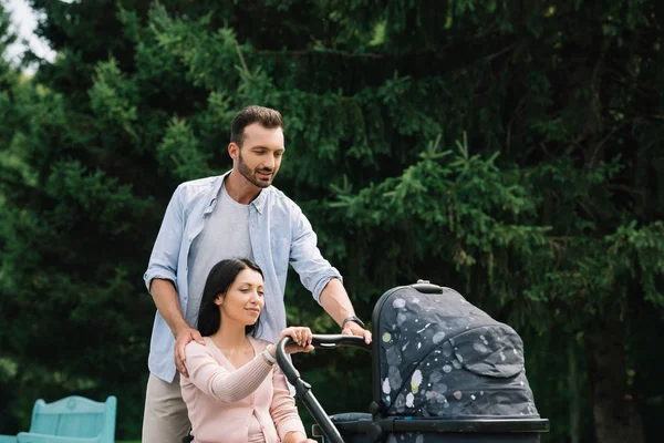 happy disabled woman and husband walking with baby carriage in park together