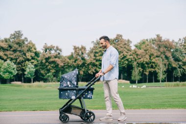 parkta bebek arabası ile yürüyen yakışıklı neşeli adam