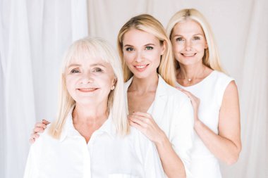 happy elegant three-generation blonde women in total white outfits clipart
